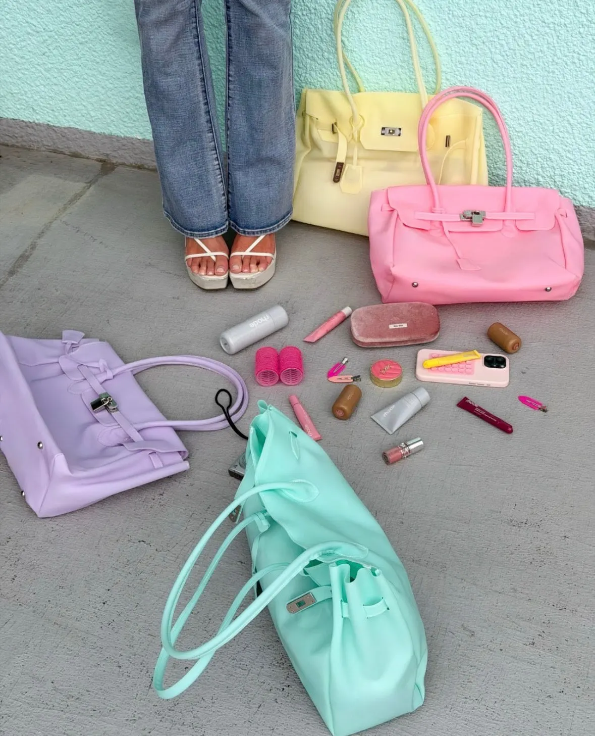Trois cabas jelly mat poudrés — lilas, menthe et rose — posés au sol avec leur contenu